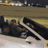 a woman is driving a white car with a yellow ferrari logo on the side