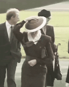 a woman in a hat is walking with a man in a suit and tie .