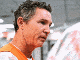 a man wearing a white shirt and an orange vest looks to the side