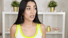 a woman wearing hoop earrings and a neon yellow tank top looks surprised