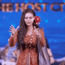 a woman with a flower in her hair stands in front of a sign that says " the host of "