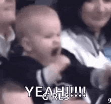 a baby is screaming in a crowd of people while a woman holds it .