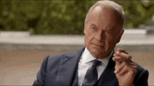 a man in a suit and tie is smoking a cigar outdoors .