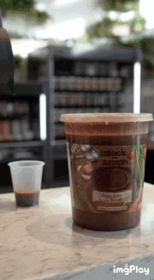 a container of stock sauce sits on a counter next to a cup