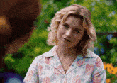 a woman wearing a floral shirt and necklace looks at another woman