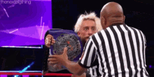 a referee is standing next to a wrestler holding a wrestling championship belt .