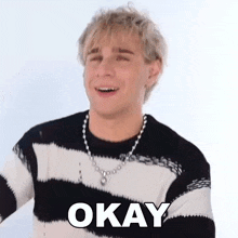 a young man wearing a striped sweater and a necklace is smiling and says okay .