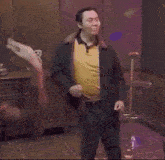 a man in a yellow shirt is dancing in a room in front of a microphone .
