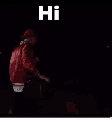 a man in a red jacket and hat is standing in the dark and says hi .