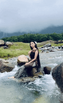 a woman with long hair is sitting on a rock in a river