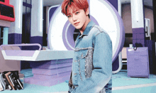 a young man wearing a denim jacket stands in front of a purple and white circle