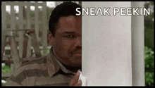 a man in a striped shirt is peeking out from behind a pole .