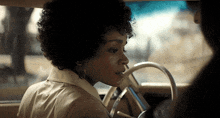 a woman with curly hair is driving a car and looking out the window