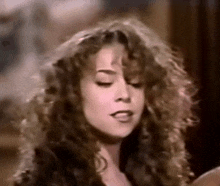 a close up of a woman with curly hair making a funny face with her eyes closed .
