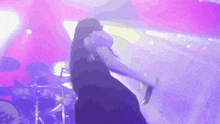 a woman is singing into a microphone on a stage with a drummer in the background