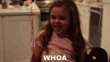 a little girl is sitting in a chair with the word whoa written on her chest .