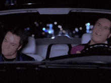 two men are sitting in a car at night and smiling