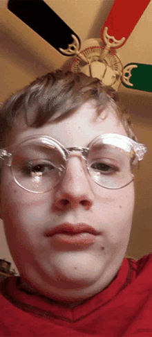 a young man wearing glasses looks at the camera with a ceiling fan behind him