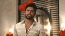 a man with a beard and a white shirt is standing in front of balloons .