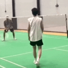 a man is playing badminton on a green court while another man watches .