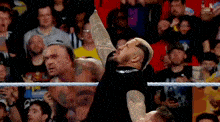 a wrestler is standing in a wrestling ring with his arms in the air .
