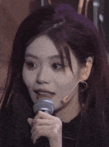a girl with purple hair is singing into a microphone with chinese writing on it