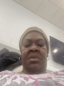 a woman wearing a beanie looks at the camera with a tv in the background