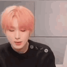 a young man with pink hair is wearing a black sweater with buttons on the shoulder .