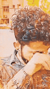 a man with curly hair and a beard is covering his face with his hand