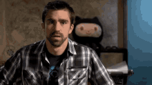 a man with a beard wearing a plaid shirt is standing in front of a stuffed animal .