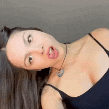 a woman in a black tank top is making a funny face and sticking her tongue out .