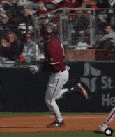 a baseball player wearing a maroon jersey and white pants is running on the field .