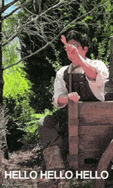 a man is sitting on a wooden bench in the woods and waving .