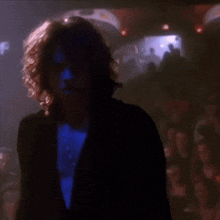 a man with curly hair and a blue shirt is standing in a dark room