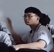 a man wearing glasses is sitting in a classroom with other students .