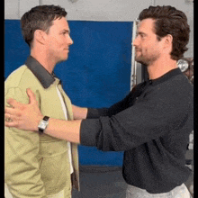 two men are hugging each other in front of a blue wall