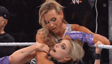 two women are wrestling in a ring with a w logo on the wall