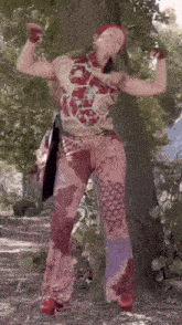 a woman is flexing her muscles while standing next to a tree in the woods .