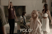 a group of women are dancing in a living room and the word yolo is on the screen