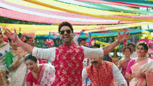 a man in a red vest and sunglasses is dancing in a crowd of people .