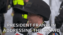a man is wearing a hat and talking into a microphone while addressing the crowd .