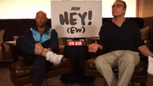 two men sit on a couch with a sign that says hey on air