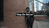 a man in a suit and tie is standing in front of a building with the words " hop on tetr.io " on it