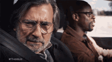 a man with glasses and a beard sits in the back seat of a car with another man