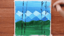 a painting of mountains with trees in the foreground on a wooden table