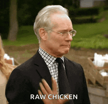 a man in a suit and tie says raw chicken with his hand