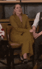 a woman in a yellow suit is sitting in a chair with her hand in the air