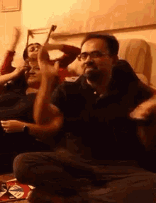 a man with glasses is sitting on the floor playing a video game while a woman watches .