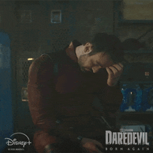 a man is sitting in a dark room with his hand on his forehead in a daredevil born again advertisement .