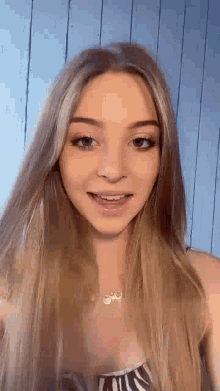 a close up of a woman with long blonde hair wearing a necklace and smiling .